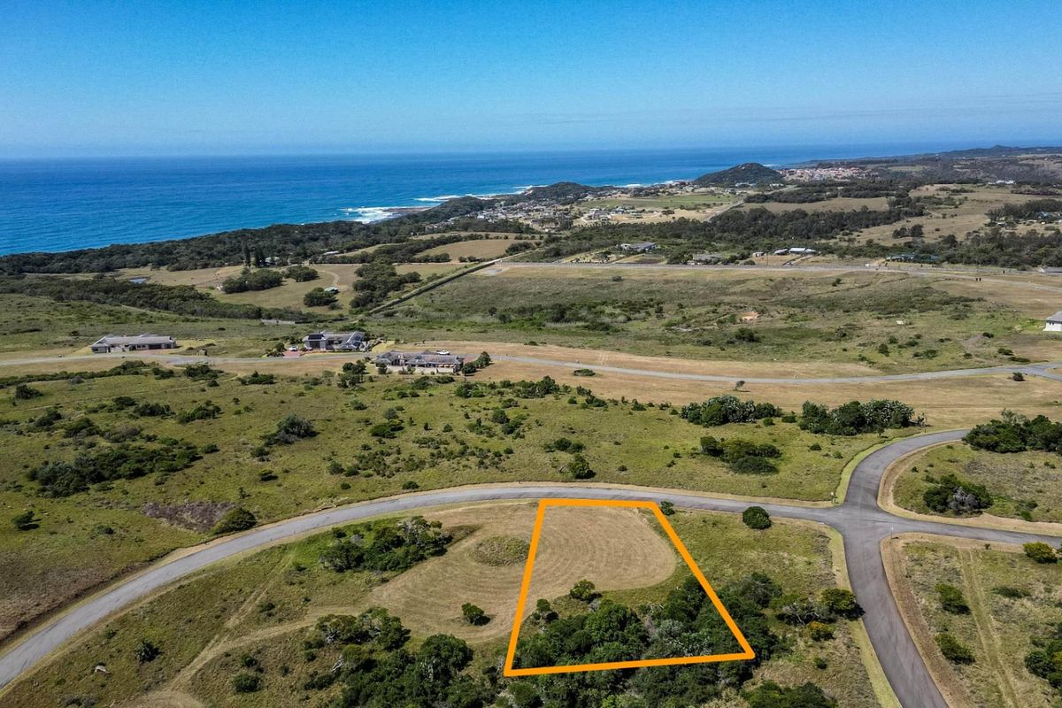 An aerial view of a vacant residential plot in a coastal estate, featuring established vegetation and proximity to the ocean.