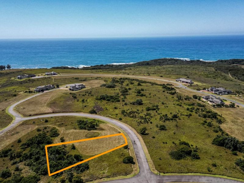 An aerial view of a vacant residential plot in a coastal estate, featuring natural vegetation and proximity to the ocean.