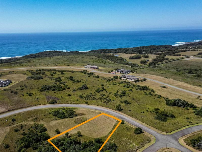 Aerial view of a vacant residential plot in a coastal estate, featuring established road access and scenic ocean views.