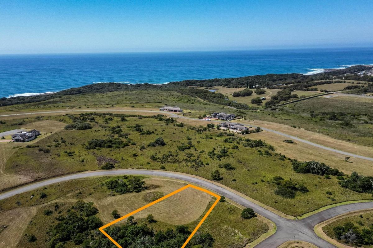 Aerial view of a vacant residential plot in a coastal estate, featuring established road access and scenic ocean views.