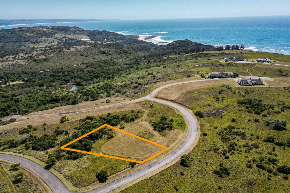 Aerial view of a vacant residential plot in a coastal estate, featuring natural vegetation and proximity to the ocean.