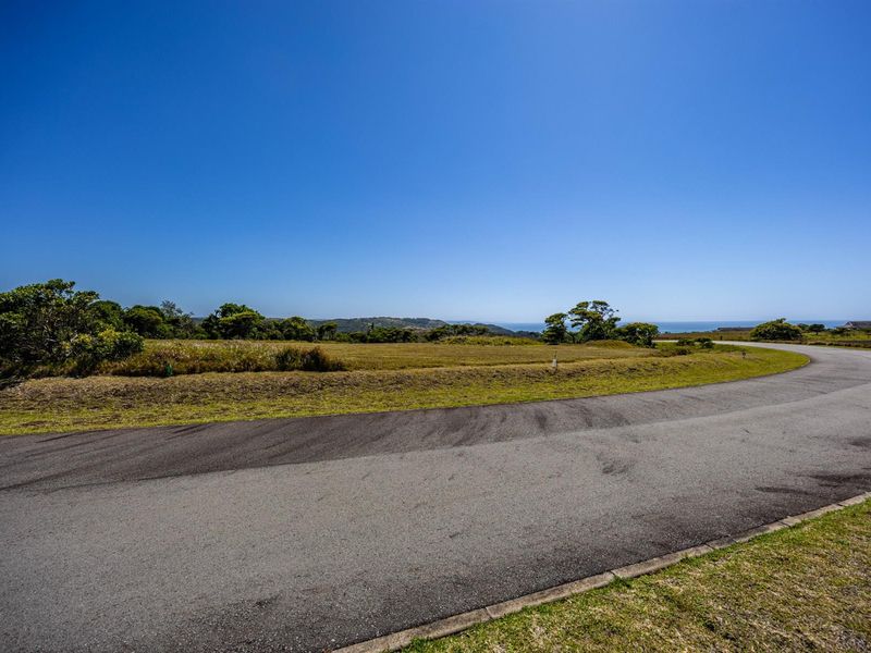 A view of a vacant residential plot featuring paved road access and scenic coastal landscape views.
