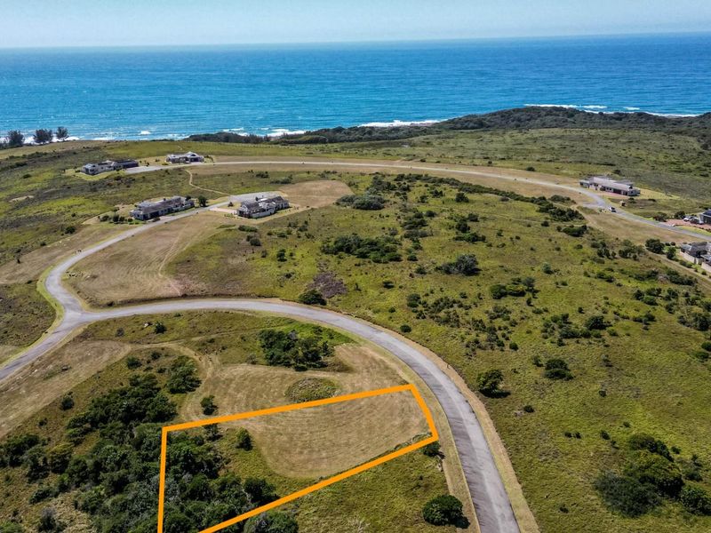 Aerial view of a vacant residential plot in a coastal estate, featuring established road access and scenic ocean views.