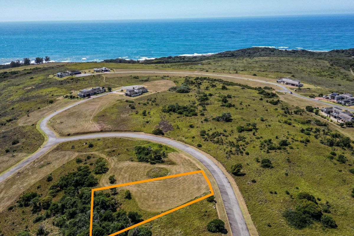 Aerial view of a vacant residential plot in a coastal estate, featuring established road access and scenic ocean views.