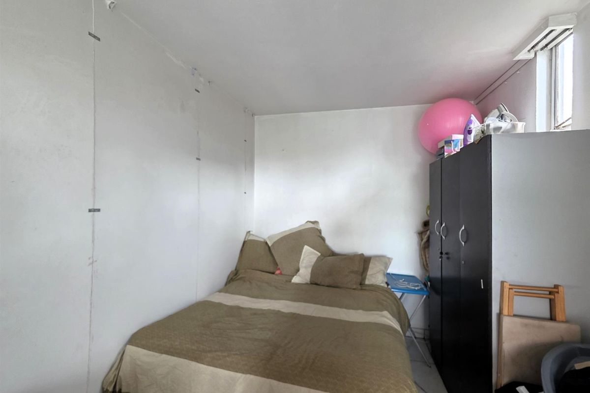 A compact bedroom featuring plain white walls with visible panel seams and a small window, offering a functional space for rest.