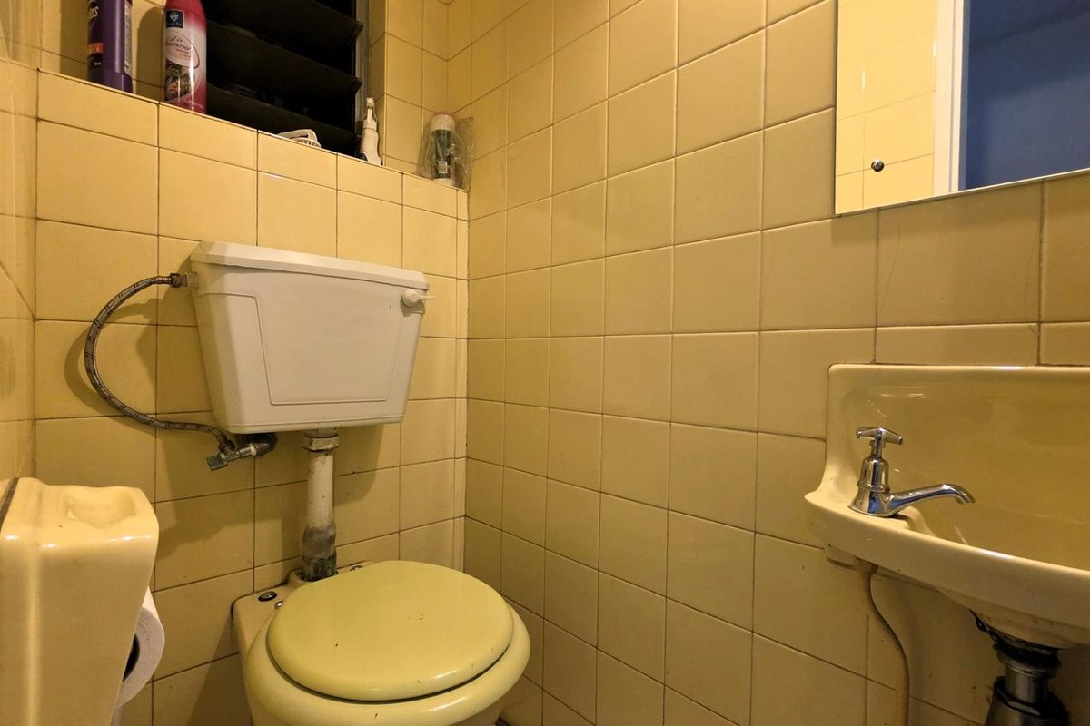 A compact, dated bathroom featuring original yellow wall tiling, a wall-mounted basin, and a standard toilet suite.