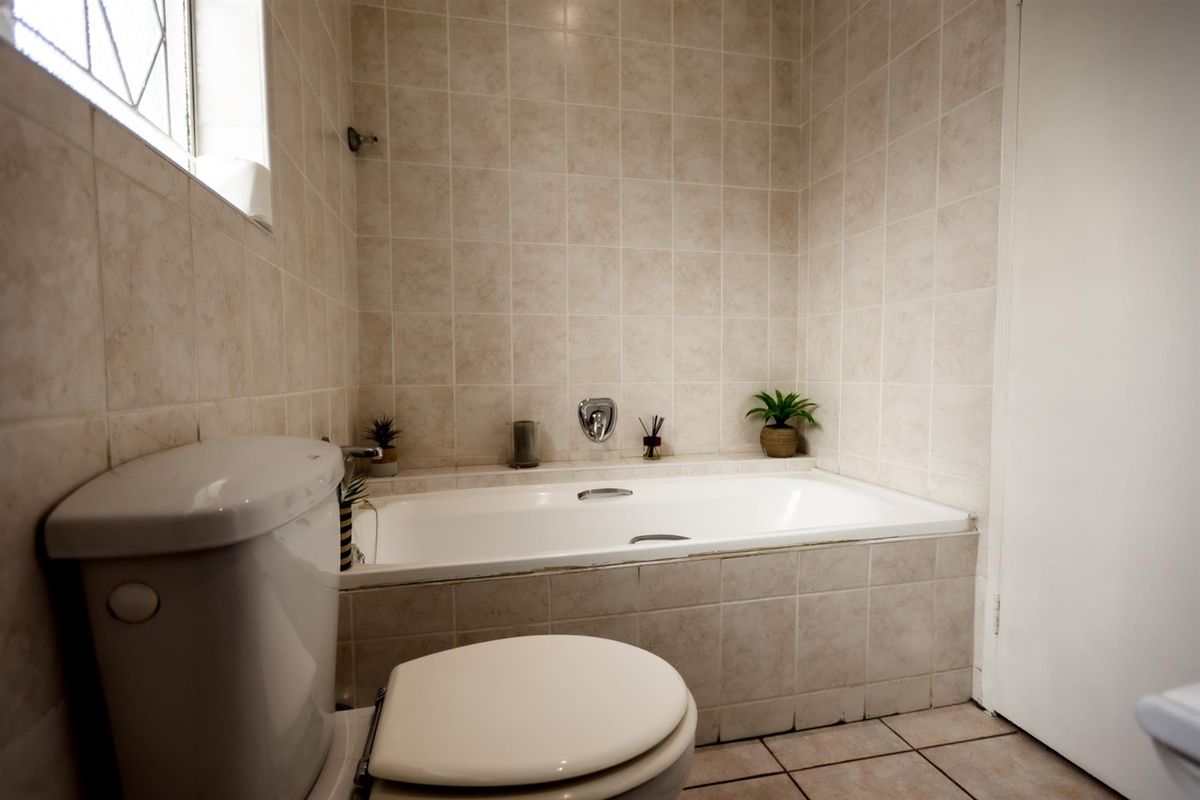 A functional bathroom featuring a built-in bathtub with tiled surround, a standard toilet, and neutral wall and floor tiling.