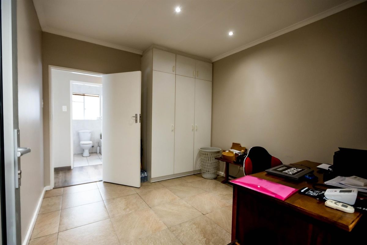 A bedroom featuring built-in cupboards, tiled flooring, and recessed ceiling lighting, with an adjoining en-suite bathroom visible through the doorway.