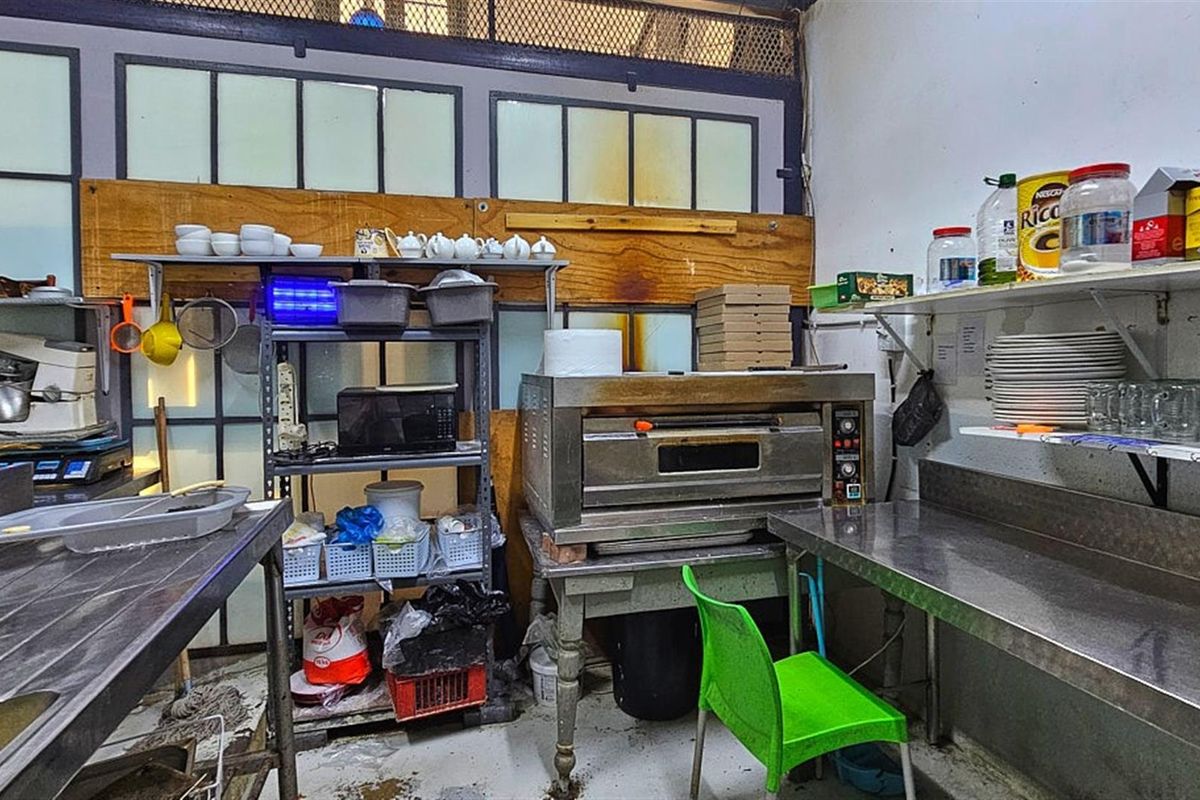 A functional commercial kitchen area featuring stainless steel prep tables, a built-in oven, and industrial shelving units for storage.
