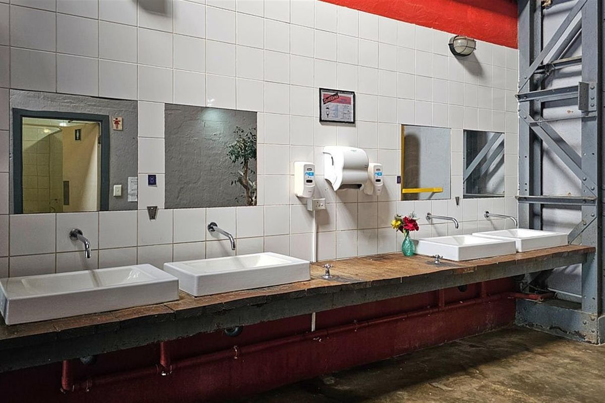 Industrial-style restaurant restroom featuring a long wooden vanity with multiple integrated vessel sinks, wall-mounted faucets, and tiled splashbacks.