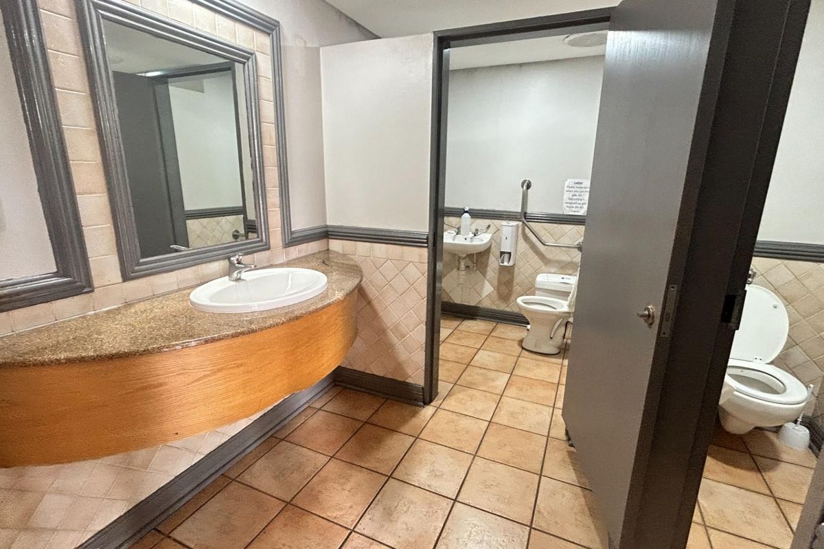 Commercial restroom facility featuring a vanity with a granite countertop, integrated sink, and separate toilet cubicles with accessible grab rails.