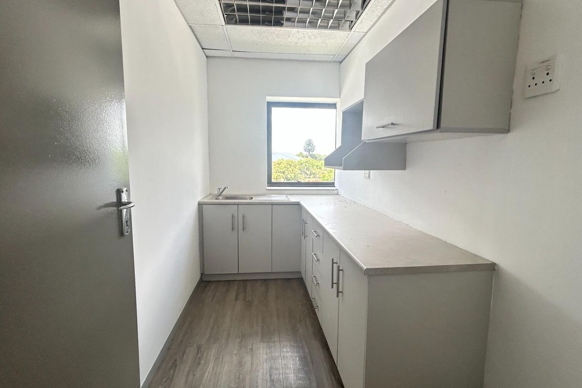 A functional kitchenette featuring built-in cabinetry, a stainless steel sink, and wood-look flooring, suitable for office or commercial use.