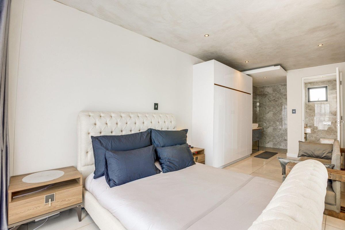 Modern bedroom featuring a concrete-look ceiling, built-in high-gloss white cabinetry, and an en-suite bathroom with stone-tiled finishes.