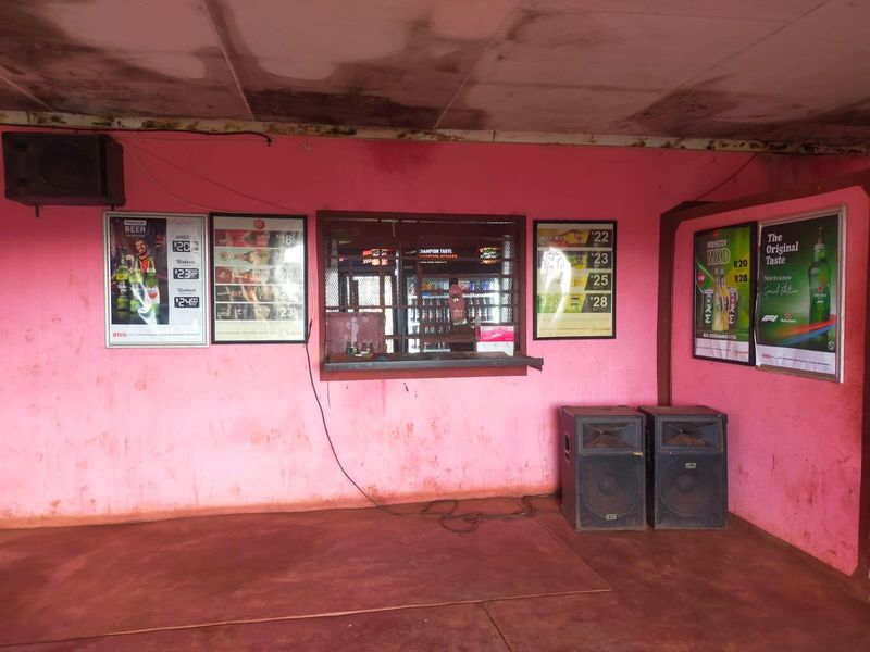 A commercial bar area featuring a serving hatch with security grille, pink painted walls, and a concrete floor, requiring maintenance and cosmetic updates.