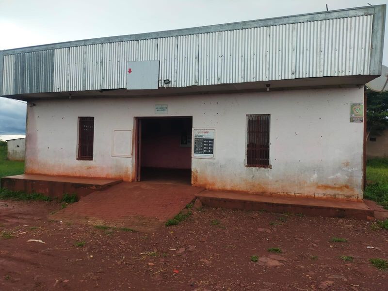 Front elevation of a commercial building featuring a corrugated metal roof, brick entrance ramp, and security-barred windows, showing signs of significant exterior wear.