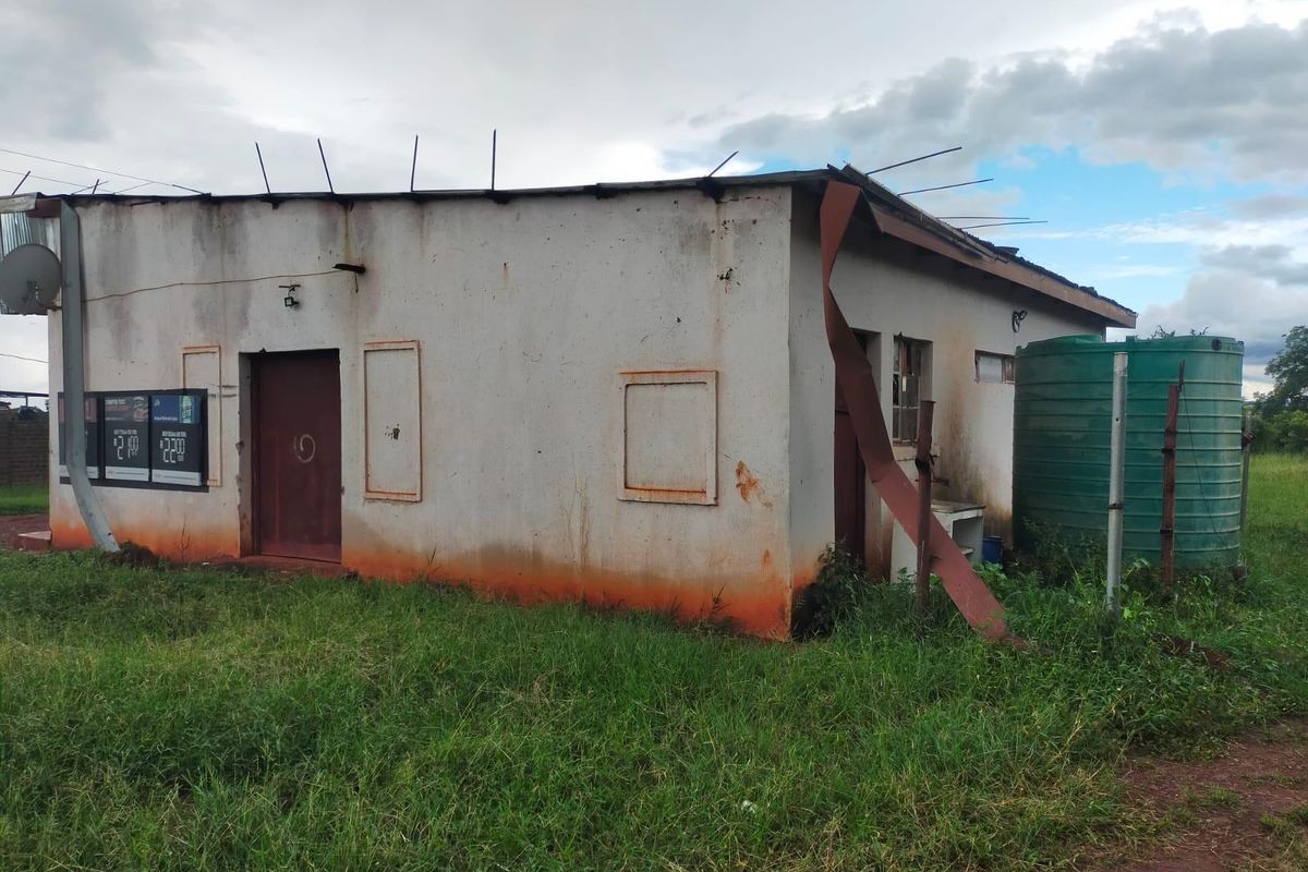 Rear exterior view of a commercial building showing significant wear, damaged roof flashing, and an external water storage tank.