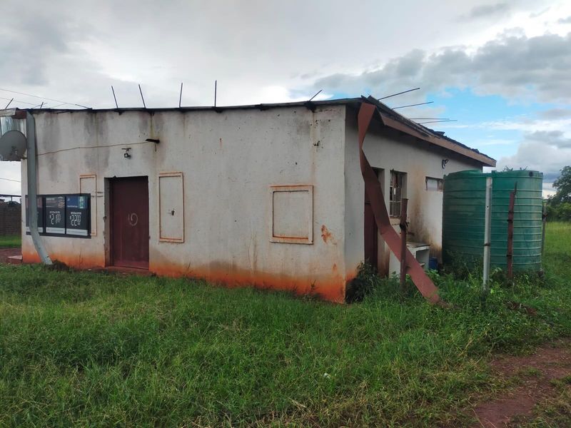 Rear exterior view of a commercial building showing significant wear, damaged roof flashing, and an external water storage tank.
