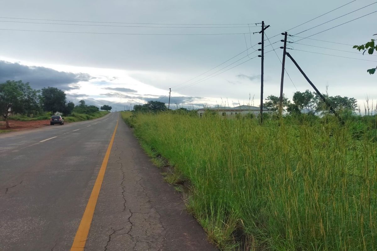 A view of the asphalt road and roadside verge adjacent to the commercial vacant land, featuring utility poles and overhead power lines.