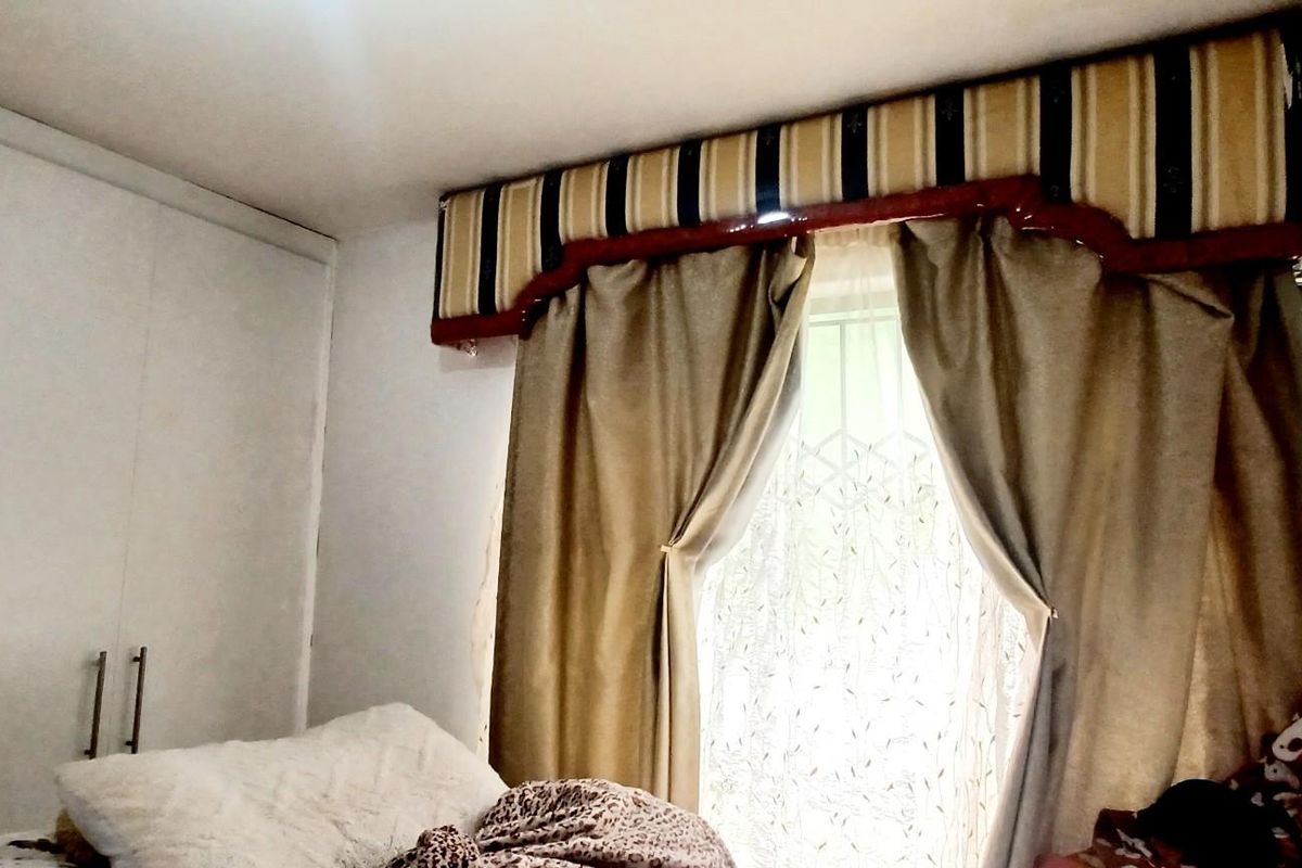 A bedroom featuring built-in cupboards and a window with a decorative pelmet and curtain arrangement.