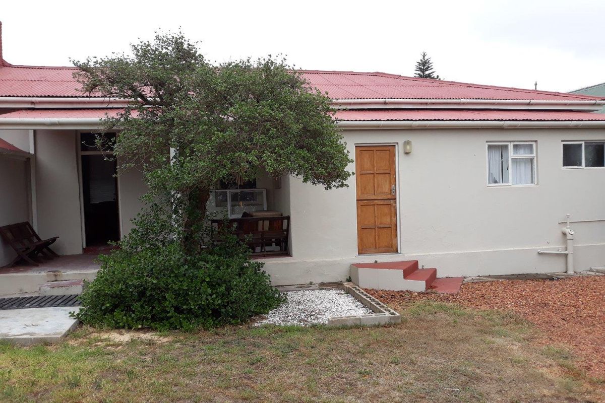 Rear exterior view of the house featuring a covered patio area, red corrugated metal roof, and access to the garden.