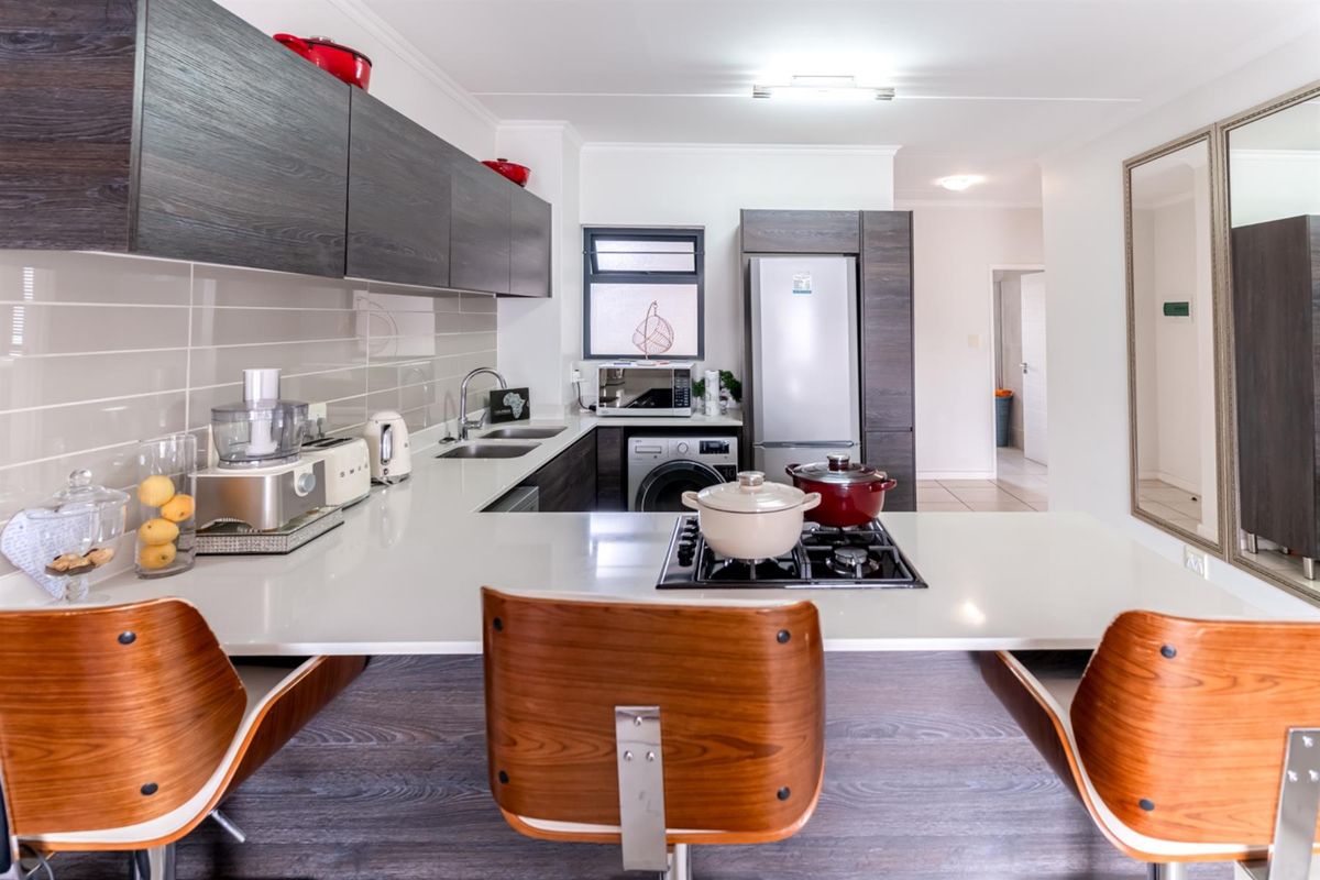 Modern kitchen featuring dark wood cabinetry, stone countertops, integrated gas hob, and a breakfast bar area with tiled backsplash.