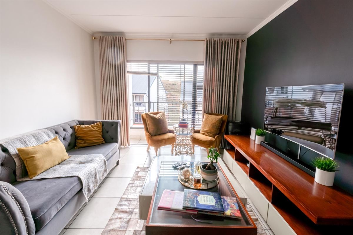 A well-maintained living room featuring tiled flooring, a feature accent wall, and large sliding doors leading to a balcony.