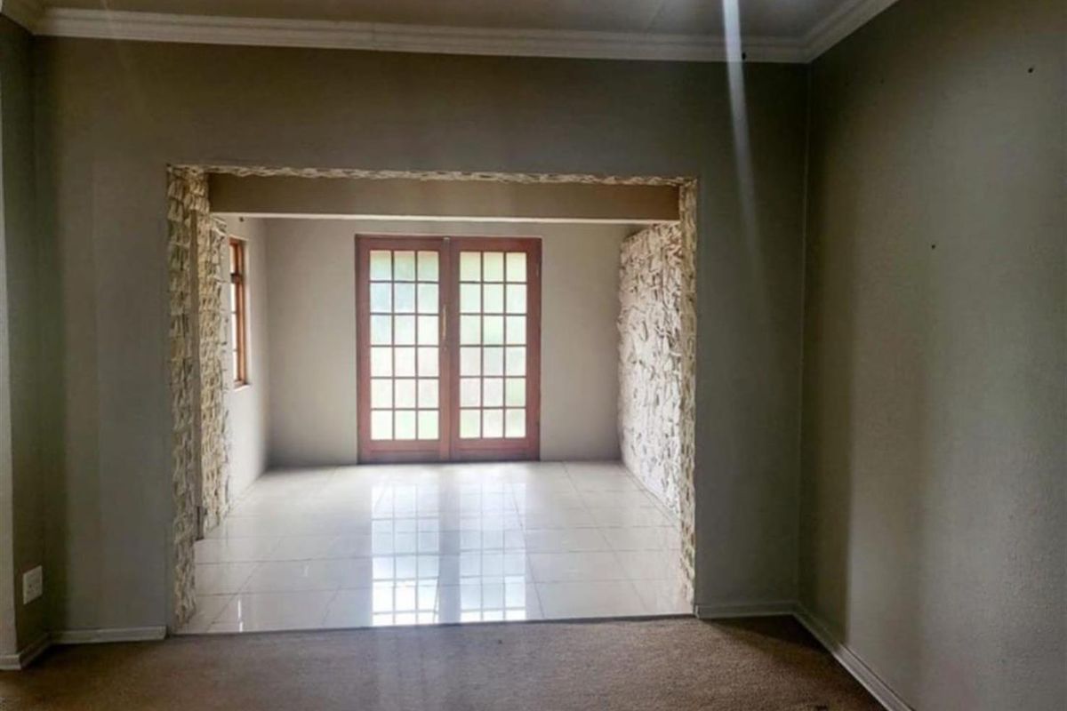 An empty living area featuring stone-clad accents, tiled flooring in the transition space, and classic french doors leading to the exterior.