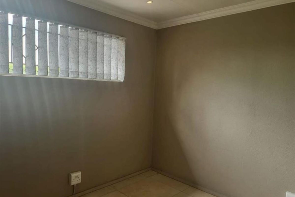 A clean, empty bedroom featuring neutral wall tones, tiled flooring, recessed ceiling lighting, and vertical window blinds.