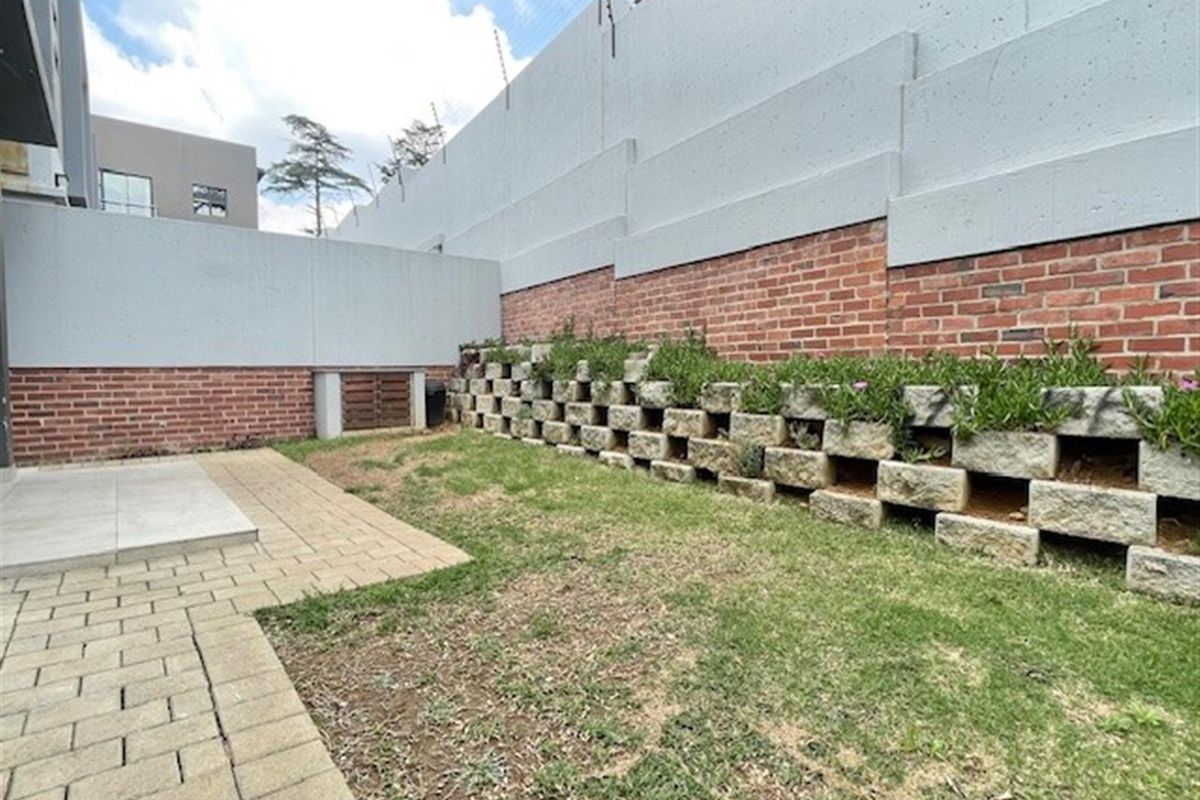 A private rear garden area featuring a paved patio, a small lawn, and a tiered brick and concrete block retaining wall.