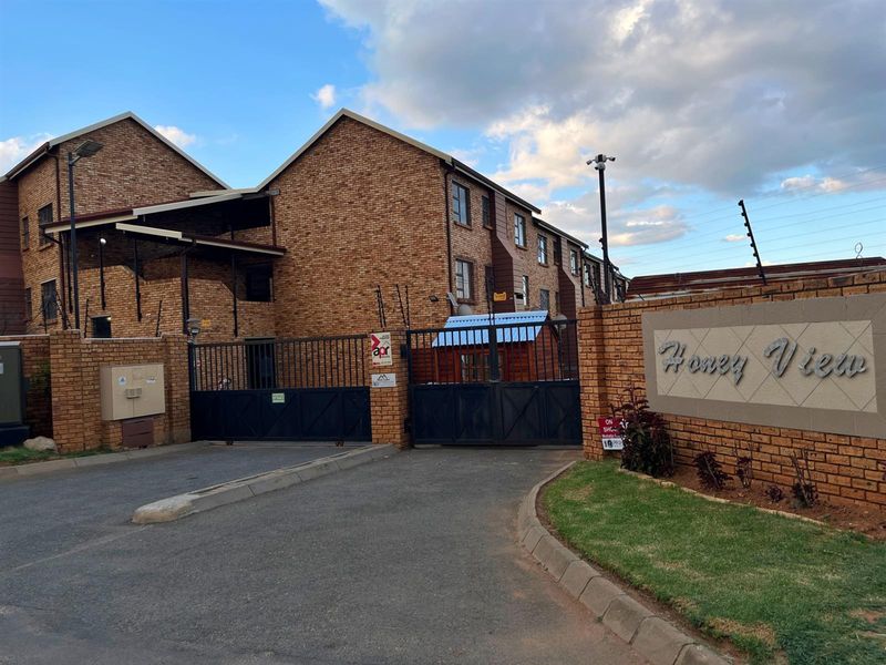 Front entrance view of the Honey View apartment complex featuring a brick facade, secure gated access, and perimeter electric fencing.