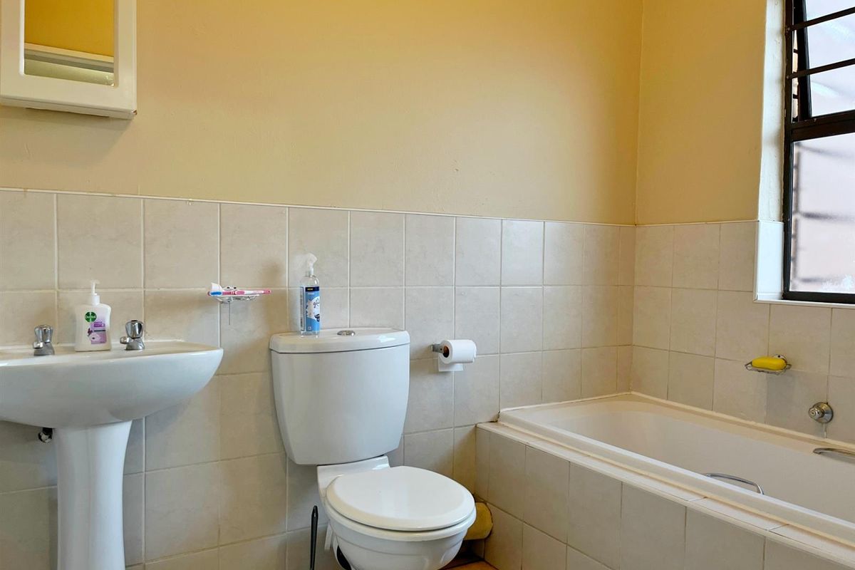A functional bathroom featuring a pedestal basin, standard toilet, and bathtub with tiled splashbacks and a window with security bars.