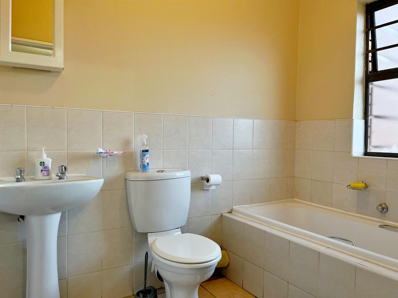A functional bathroom featuring a pedestal basin, standard toilet, and bathtub with tiled splashbacks and a window with security bars.