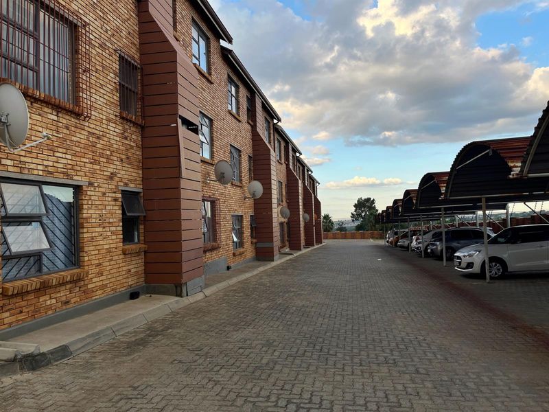 Exterior view of a face brick apartment complex featuring a paved driveway and covered parking bays.