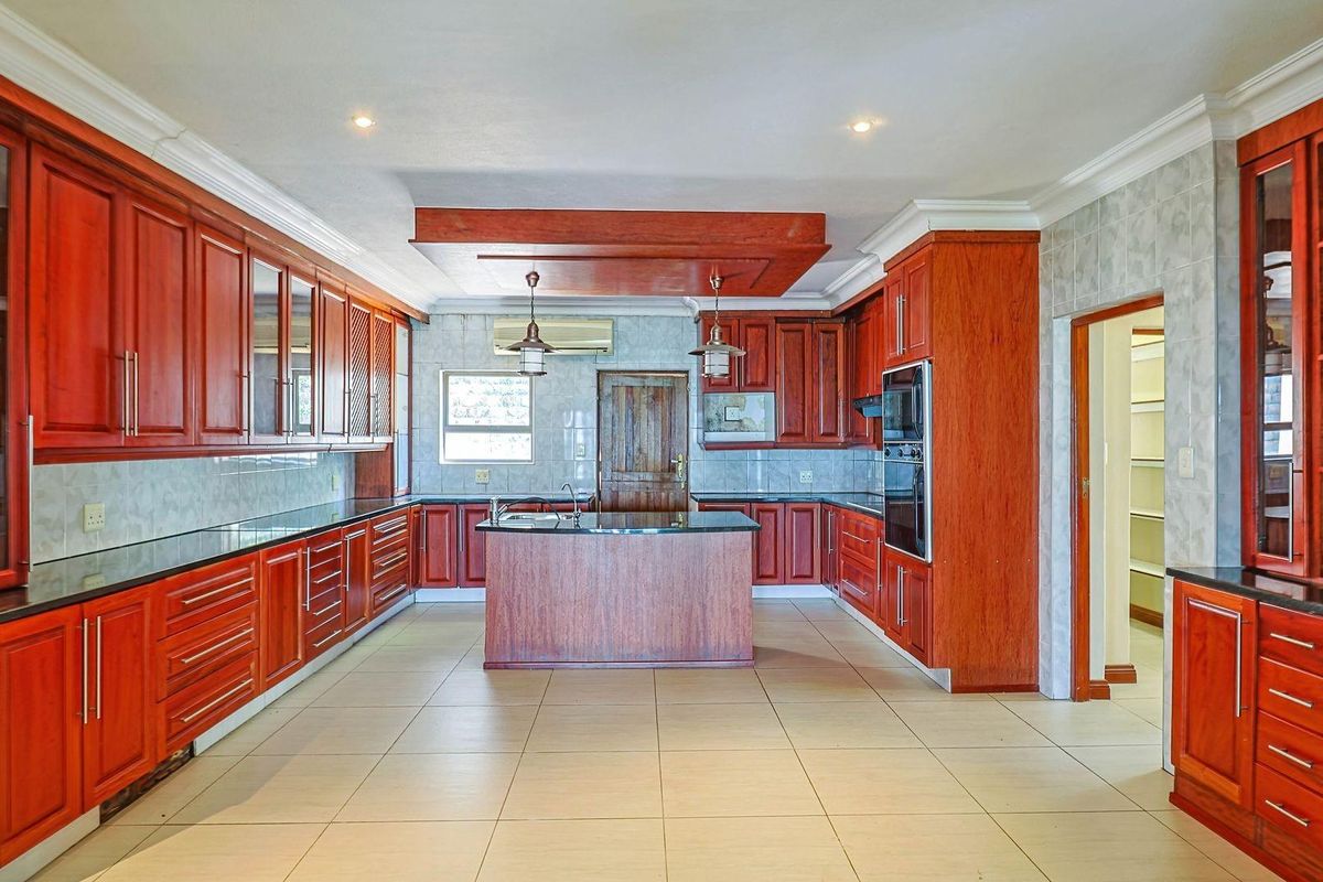 Spacious kitchen featuring extensive cherry wood cabinetry, granite countertops, a central island, built-in oven, and tiled flooring with an adjacent pantry area.