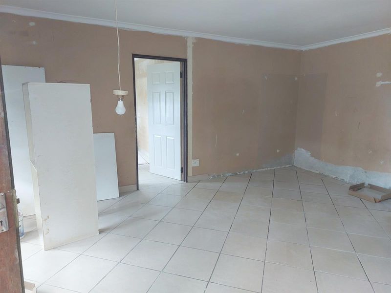 An empty living room space featuring tiled flooring, unfinished wall surfaces, and a single pendant light fixture, ready for renovation and finishing.