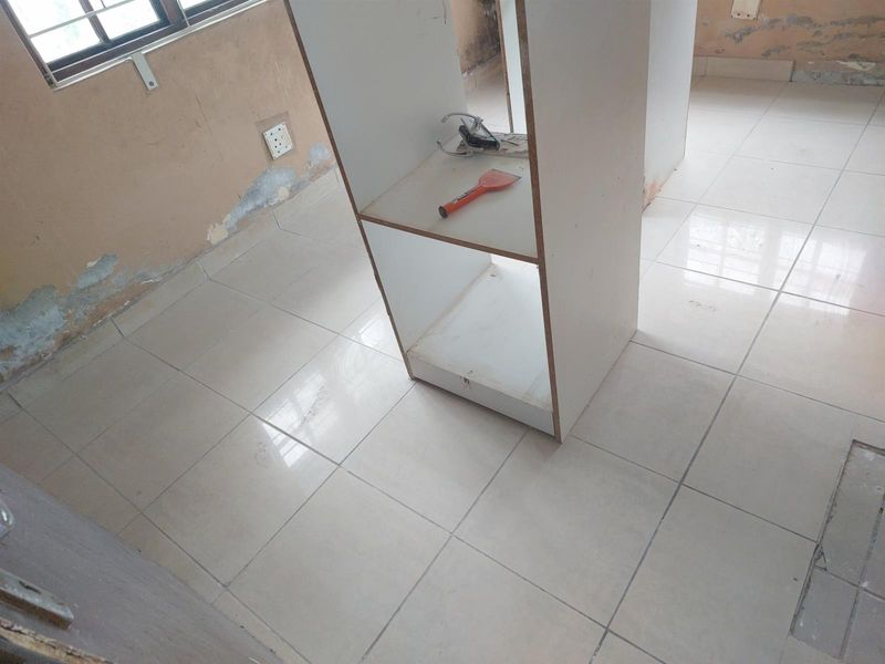 A room interior featuring tiled flooring and a central built-in shelving unit, currently requiring wall repairs and cosmetic updates.
