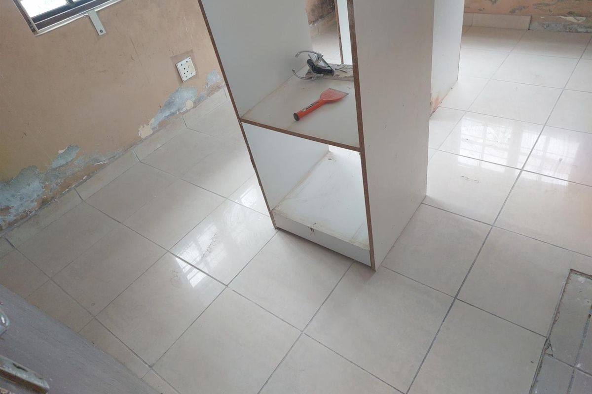 A room interior featuring tiled flooring and a central built-in shelving unit, currently requiring wall repairs and cosmetic updates.