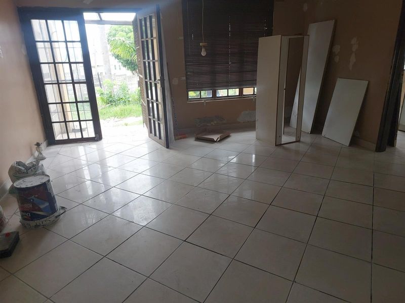 An empty living area featuring tiled flooring, large glass-paned double doors leading to the garden, and window blinds.
