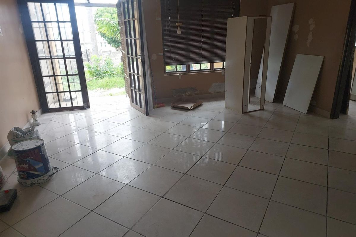An empty living area featuring tiled flooring, large glass-paned double doors leading to the garden, and window blinds.