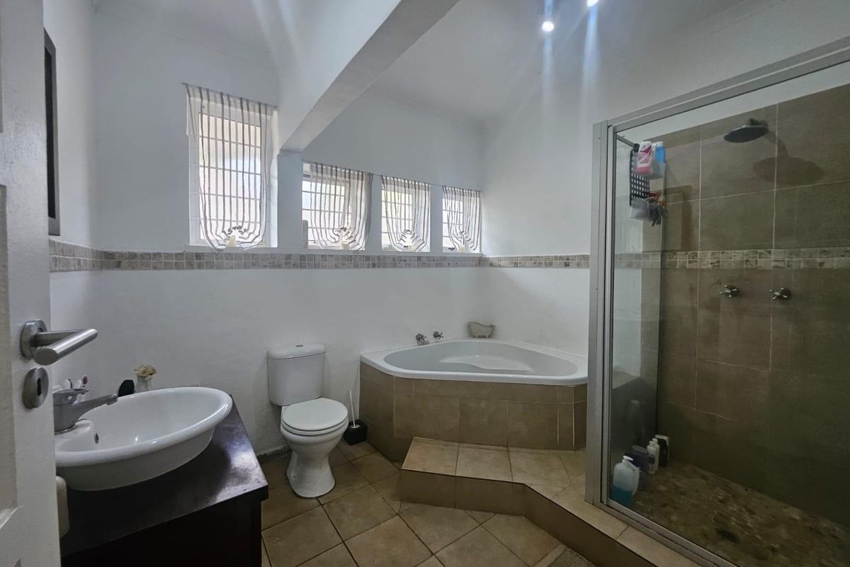A functional bathroom featuring a corner bathtub, separate glass-enclosed shower, vanity basin, and neutral floor tiling.