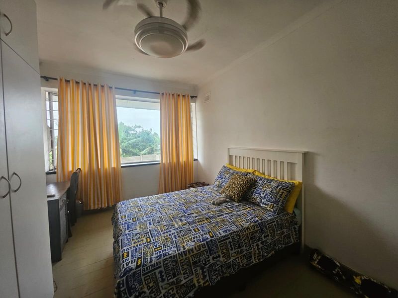 A functional bedroom featuring a built-in wardrobe, ceiling fan, and large window providing natural light.