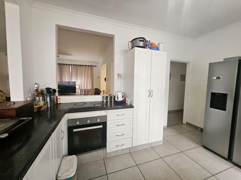 A functional kitchen featuring white cabinetry, granite countertops, a built-in oven, and an electric hob, with a convenient serving hatch to the living area.