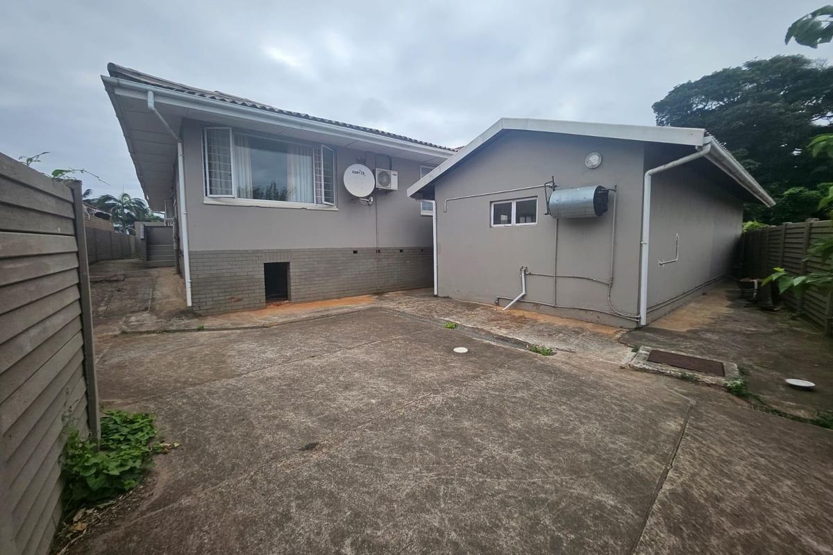Rear exterior view of the property featuring a concrete courtyard, external geyser, and air conditioning unit against a grey painted facade.