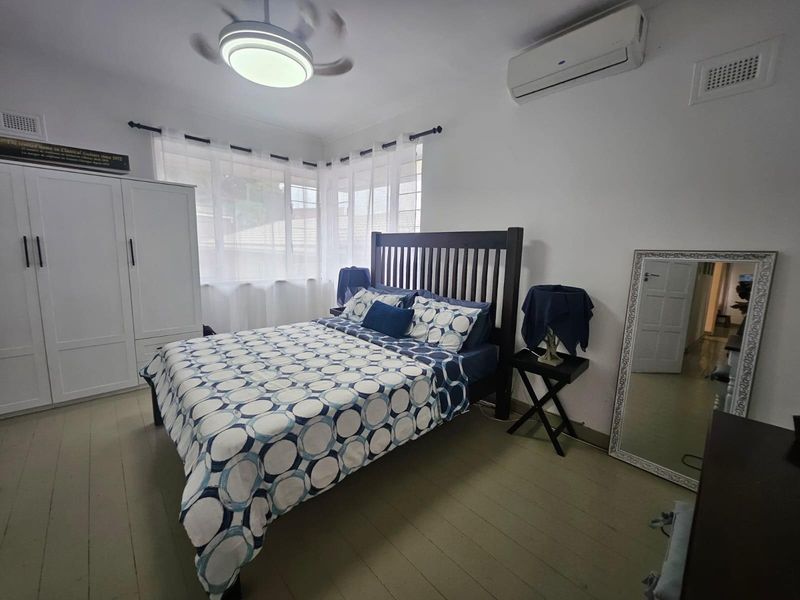 A well-lit bedroom featuring timber flooring, a built-in wardrobe, a ceiling fan, and a split-system air conditioning unit for climate control.