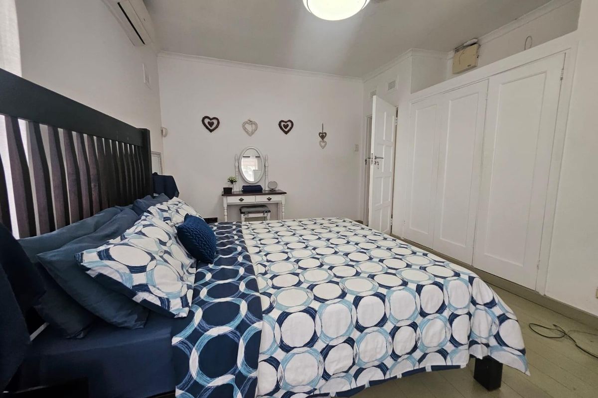 A well-lit bedroom featuring built-in white cupboards, an air conditioning unit, and neutral finishes, providing a functional and comfortable living space.