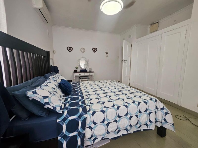 A well-lit bedroom featuring built-in white cupboards, an air conditioning unit, and neutral finishes, providing a functional and comfortable living space.