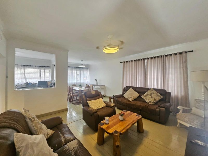 Open plan living and dining area featuring timber flooring, a ceiling fan, and a convenient pass-through window connecting to the kitchen.