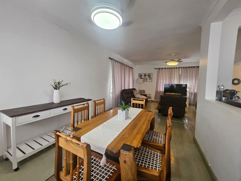An open-plan living and dining area featuring painted timber flooring, ceiling fans, and neutral wall finishes, providing a functional and connected living space.