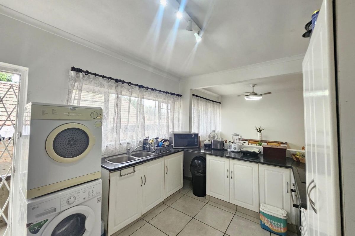 Functional kitchen featuring white cabinetry, dark countertops, double sink, and tiled flooring, with integrated laundry appliances and ample natural light.