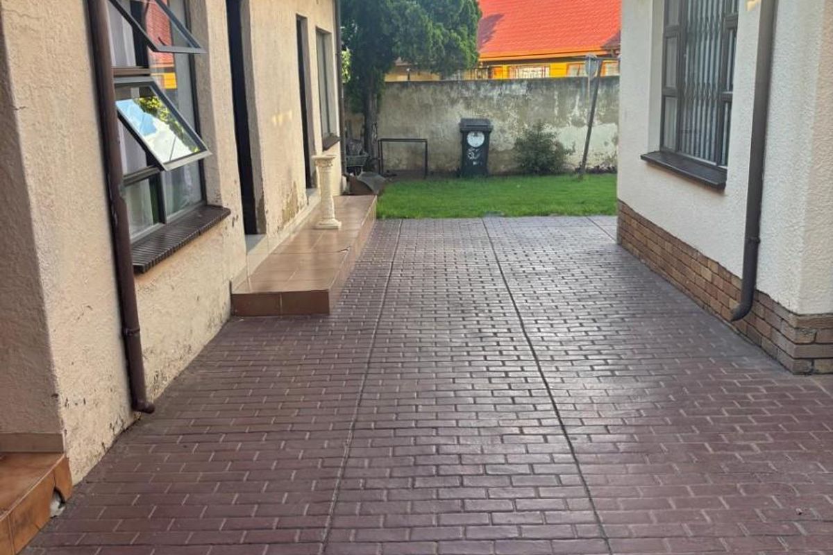 A paved side courtyard area between two building structures, featuring brick paving, exterior wall finishes, and access to a small rear garden space.
